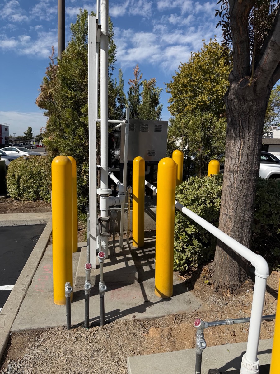 Yellow steel bollards protecting above-ground piping and a riser at a fueling site