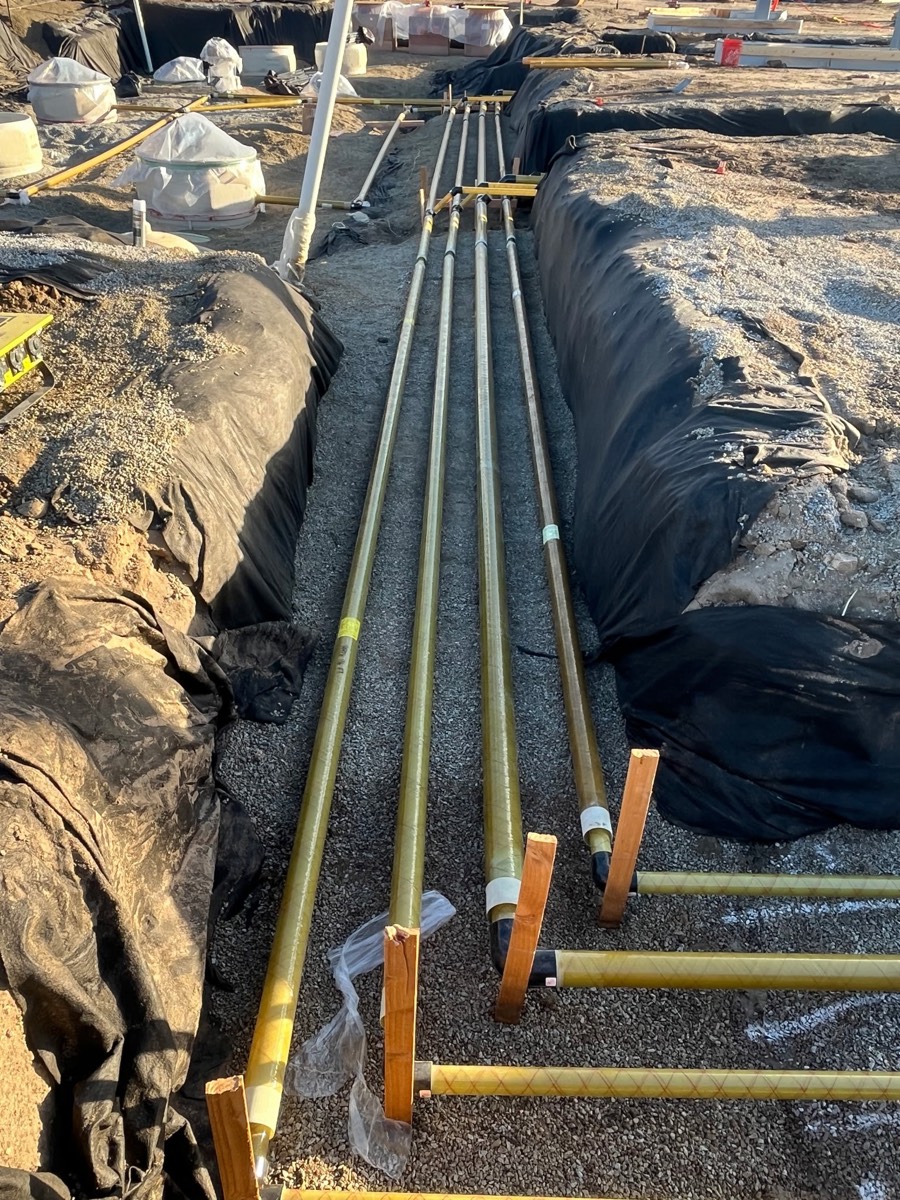 Product piping lines running down a gravel-bedded trench toward wrapped sumps, late in the day