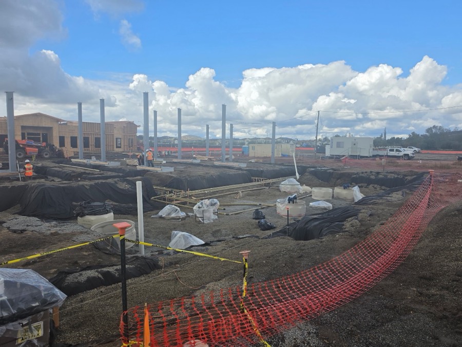 Canopy columns and trenching across a fueling station site, with the site office and crew trucks behind