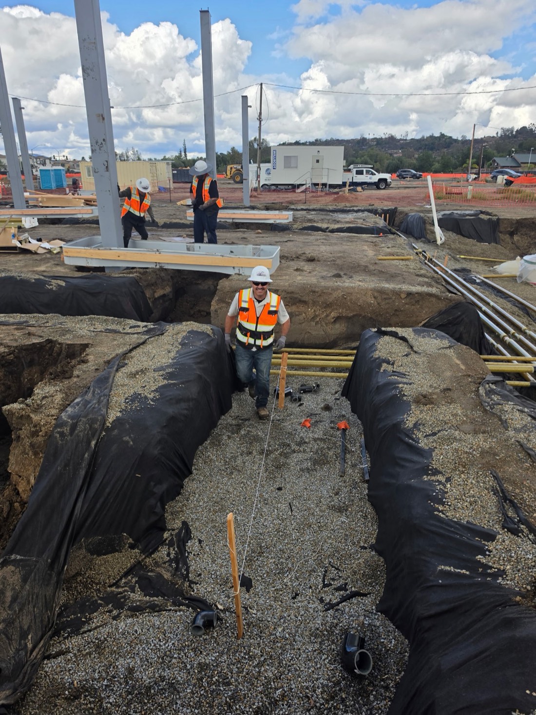 Frank Vasquez, owner of Vasquez Pipeline and Fuel Construction, standing in a product piping trench, crew and canopy columns behind