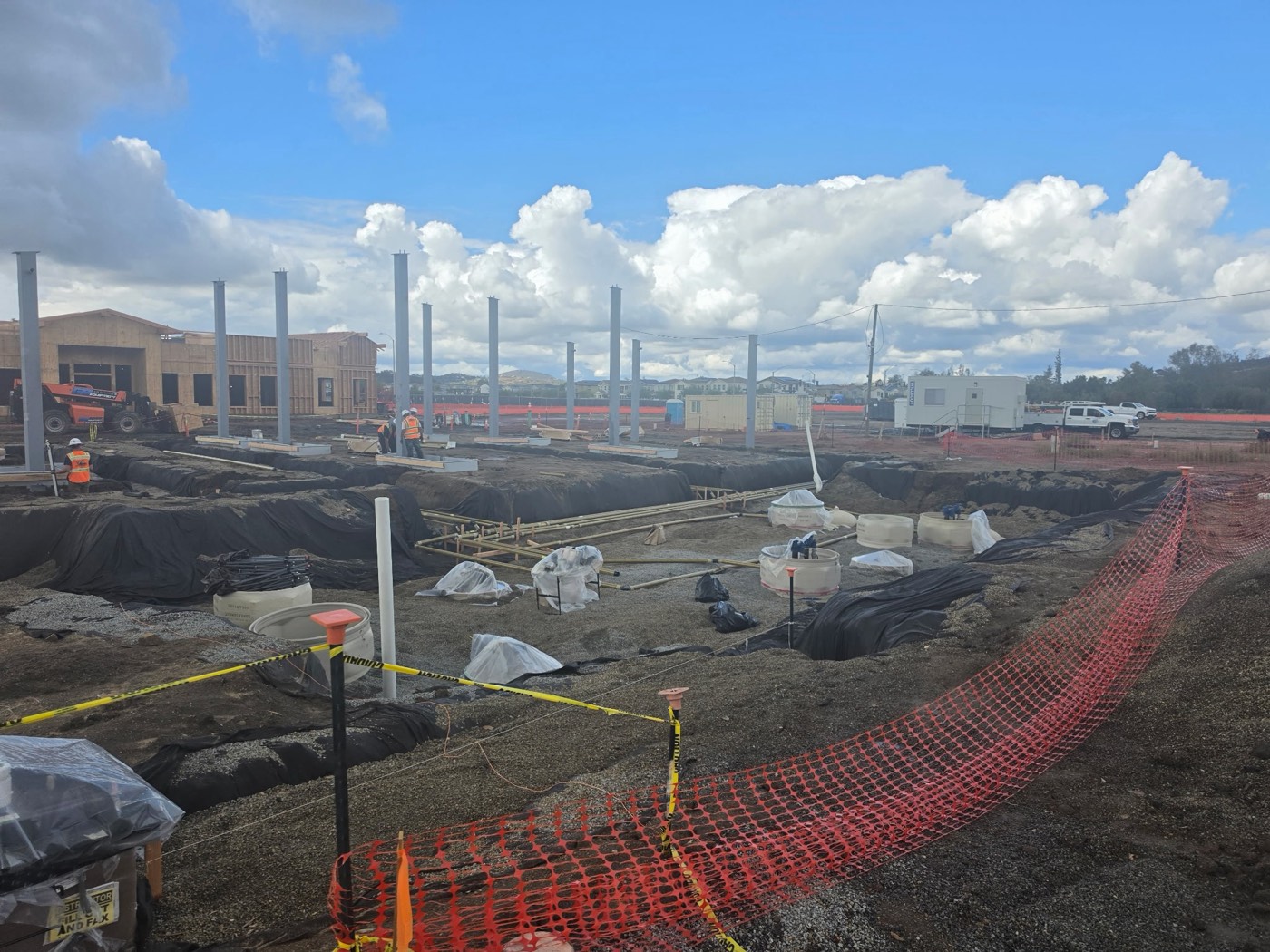 Canopy columns and trenching across a fueling station site, with the site office and crew trucks behind