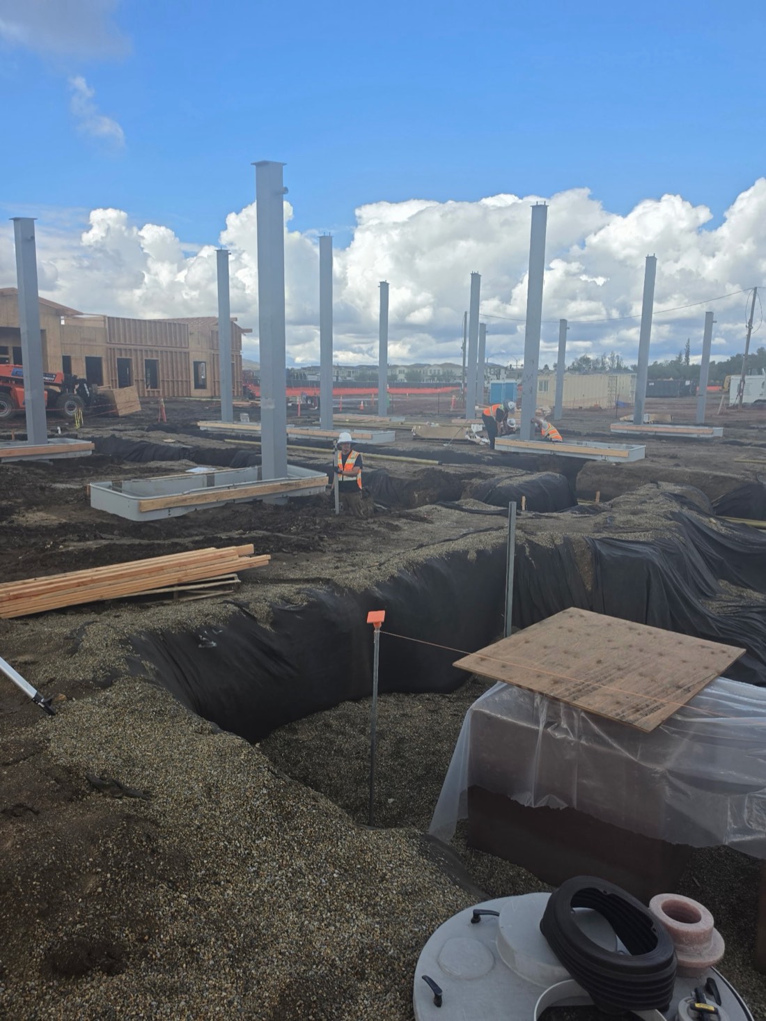 Canopy steel columns on their footings beside lined trenches, crew at work