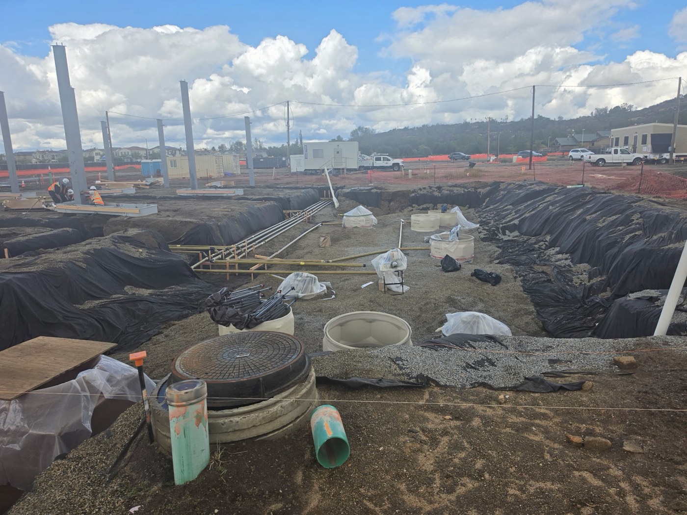 Product piping and sumps laid out in a gravel-bedded trench at a fueling station build, manhole cover in the foreground